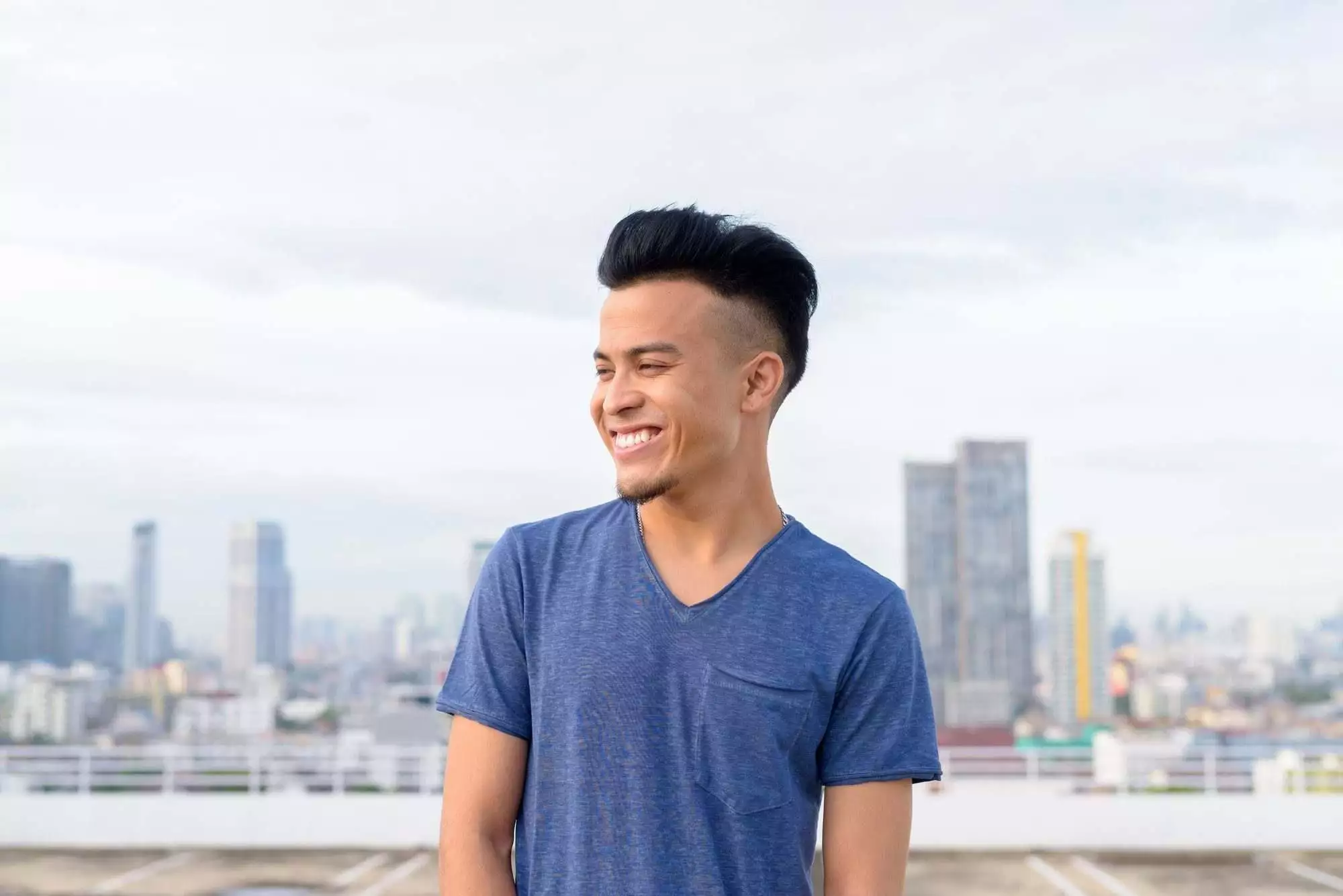 Happy young handsome multi ethnic man thinking against view of the city